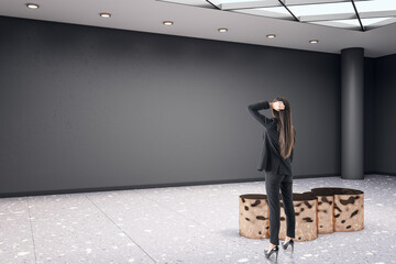 Poster - Businesswoman standing in modern exhibition hall interior with shiny golden seat and empty mock up place on concrete wall. Gallery and art concept.