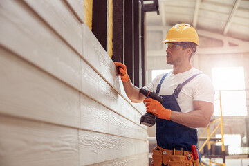 Wall Mural - Handsome young man builder installing exterior wood siding