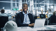 © Gorodenkoff - Portrait of a Happy Young African American Engineer Working on Laptop Computer in an Office at Car Assembly Plant. Industrial Specialist Working on Vehicle Parts in Technological Development Facility.