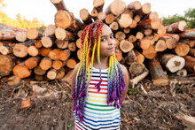 Girl In Front Of Pile Of Logs Glances At Camera