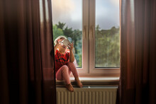 Small Child Sitting On Windowsill And Drinking From Cup