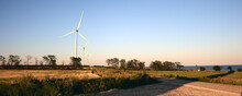 Wind Turbine Panorama Landscape In A Field On A Sunny Summer Day. Renewable Energy Plants. Wind Farm Along The Coast At Sunset With Blue Sky And Without Clouds
