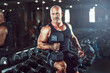 Bald male bodybuilder holds dumbbells in arms while posing in gym in dark. Concept of bodybuilding.