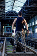 © Andrej - Young rebel in abandoned marshalling yard, with a metal bar in his hand, looking down the rails facing the locomotive. People struggle for freedom concept.