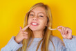 © Roquillo - caucasian kid girl wearing blue knitted sweater over yellow background   holding an invisible aligner and pointing to her perfect straight teeth. Dental healthcare and confidence concept.
