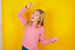 Photo of upbeat caucasian little kid girl wearing long sleeve shirt over yellow background has fun and dances carefree wear being in perfect mood makes movements. Spends free time on disco party