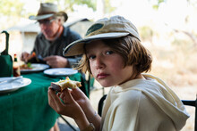 Young Boy Eating A Piece Of Toast At A Table In A Safari Camp