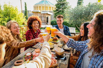 Group of multiethnic happy friends living healthy lifestyle and relaxing while drinking beer at outdoor pub restaurant - Young people enjoying drinks during happy hour at bar