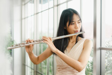 A Female Flutist Performs On Her Instrument. A Young And Elegant Asian Woman Plays The Flute