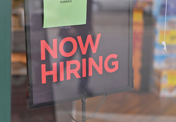 Sign on door, now hiring in red lettering