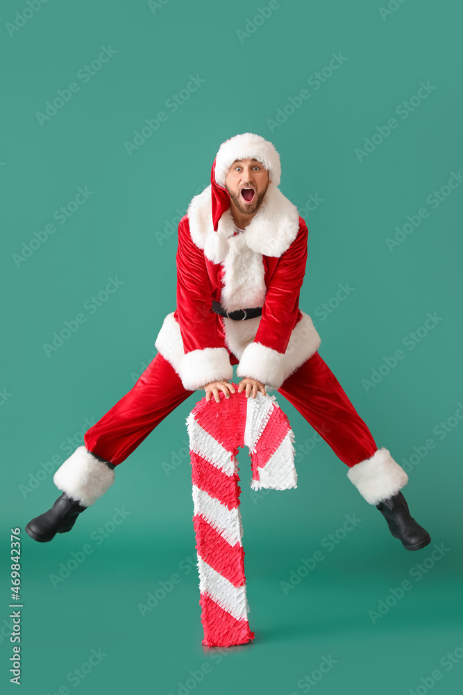 Santa Claus with candy cane pinata jumping on green background
