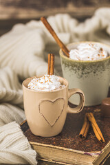 Two cups of coffee or hot chocolate with cream and cinnamon on an old book on wooden background, vertical