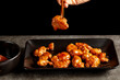A person is eating delicious mandarin orange chicken, a Chinese American dish using wooden chopsticks. The sauce is served in porcelain bowl. Dark background. Angled side view image
