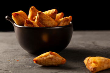 Dark background low light image showing a closeup view of traditional indian samosa, a fried triangular pasty filled with savory ingredients such as chicken and vegetables.