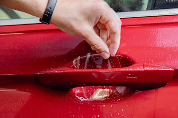 Closeup master installation on in risk zone under handles red car. Paint protection is vinyl film