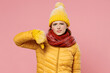 Sad irritated distempered unnerved aggrieved young woman 20s years old wear yellow jacket hat mittens showing thumb down dislike gesture isolated on plain pastel light pink background studio portrait