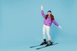 Full body skier beginner fun cool woman wearing warm purple padded windbreaker jacket ski goggles mask spend extreme weekend in mountains skiing leaning back isolated on plain blue background studio