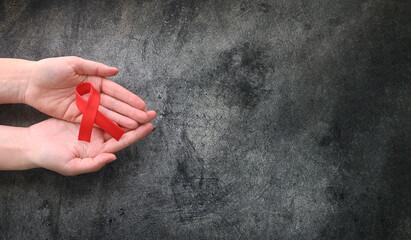 Wall Mural - Concept World AIDS Day. Hands of woman holding red ribbon on black background. Blood transfusion and donation. Hemophilia day. World Health Day. Layout. Copy space. Banner