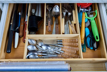 Wooden cutlery tray is divided into compartments and placed in drawer of kitchen table.