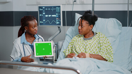 Doctor and patient looking at horizontal green screen on tablet in hospital ward. Specialist and young woman using isolated background and mockup template on device with chroma key