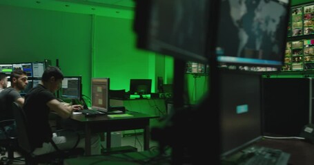 Male workers sitting near computers on monitoring room and working . Programmers or engineers using many laptops , computers , searching , following information and statistics . Cyber security office 