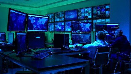 Male workers sitting near computers on monitoring room and working . Programmers or engineers using many laptops , computers , searching , following information and statistics . Cyber security office 