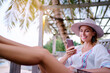 Vacation and technology. Young pretty woman in hat using smartphone sitting at beach cafe bar.
