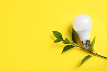 Wall Mural - Light bulb and branch with green leaves on yellow background, flat lay. Space for text