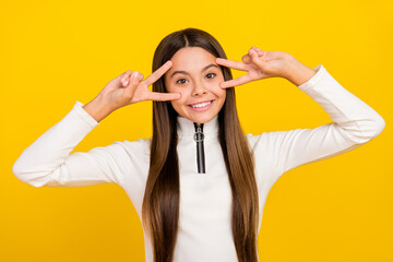 Canvas Print - Photo of funny charming student girl wear white zip shirt smiling showing two v-signs cover eyes isolated yellow color background