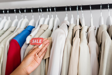 Wall Mural - cropped view of african american woman holding sale tag near clothing in boutique