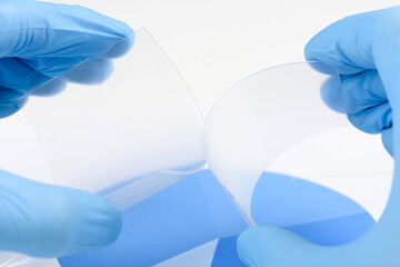 Scientist hold and bend two pieces of flexible transparent plastic like material in laboratory. Concept of research and discovery of new material.