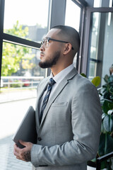 Sticker - asian businessman holding laptop while looking through window in office