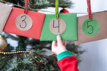 Little Girl Hand Taking Envelope Numbered 4 Of Homemade Advent Calendar Near Christmas Tree. Selective Focus