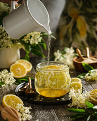 Wall Mural - homemade elderflower juice and syrup on wooden table, action shot with wooman hand