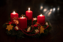 Decorated Advent Wreath From Fir Branches With Red Lit Candles, Christmas Balls And Star Cookies, Some Blurred Lights In The Dark Background, Copy Space, Selected Focus