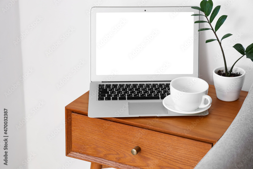 Laptop on wooden bedside table near light wall