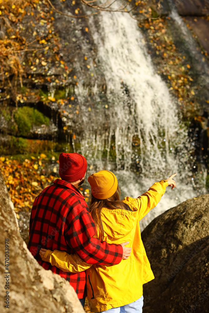 Loving couple looking at waterfall on warm autumn day