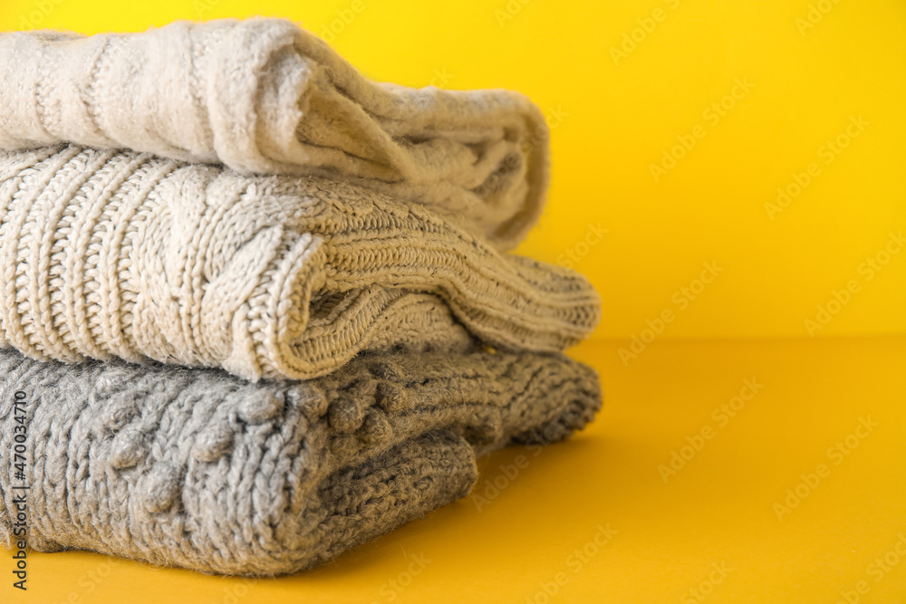 Stack of knitted sweaters on color background, closeup