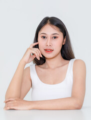 Wall Mural - Portrait close up studio shot of millennial Asian short black hair model wearing makeup red lip in tank top undershirt sitting at table posing holding hand on cheek look at camera on white background