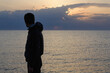 © ruslanshug - memories concept of silhouette of adult male in jacket with hood standing on sea shore looking at beautiful sky on ocean twilight dusk