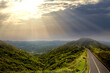 Beautiful sunset with sun rays over the contours of the mountains and a road along the top of the mountain on the background of clouds and sky