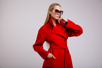 High fashion photo of a beautiful elegant young woman in a pretty red autumn coat, stylish sunglasses posing on white background. Studio Shot. Slim figure.