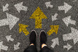 2025 Female foots in black boots standing on road with arrow markings pointing in different directions with three options for arrow direction, left, right or move forward, decision making