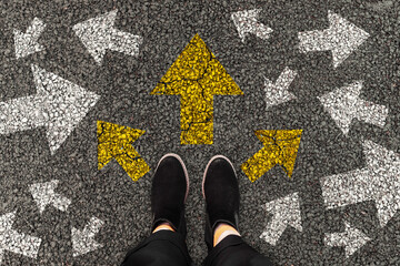 2025 female foots in black boots standing on road with arrow markings pointing in different directio