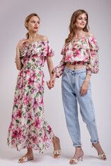 Wall Mural - Two high fashion models in long dress with a red floral pattern, blouse, blue jeans. Beautiful young women. Studio shot, portrait. White background.  Slim figure. Make up, hairstyle