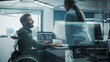 © Gorodenkoff - Disability-Friendly Office: Brilliant IT Programmer with Disability in a Wheelchair Talks with Colleague while Working on Computer. Software Engineers Develop Innovative App, Program.