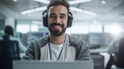 Poster - Office: Portrait of Happy IT Programmer Wearing Headphones Working on Desktop Computer, Looking at Camera and Smiling. Male Software Engineer Developing App, Video Game. Listening to Podcast, Music