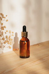 Wall Mural - Amber dropper bottle with serum or essential oil on natural wooden background with daylight. Skincare products , natural cosmetic with with dry plants. Beauty concept for face body care