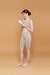 © LIGHTFIELD STUDIOS - Side view of smiling barefoot woman holding tube with cosmetic lotion on beige background