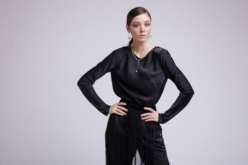 High fashion photo of a beautiful elegant young woman in a pretty black blouse, fringe trousers, accessories over white background. Studio Shot. Gathered dark hair. Slim figure